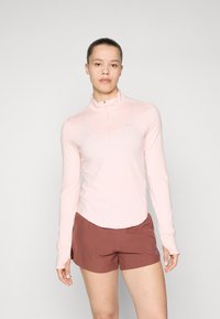Lys rosa langermet topp med kvart glidelås og Nike-logo, sammen med brune treningsshorts, som viser glatt, elastisk stoff.