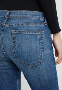 Jeans de mezclilla azul oscuro con un diseño ajustado, que cuentan con un bolsillo trasero con un pequeño logo. La tela tiene una textura suave y sin patrones visibles.