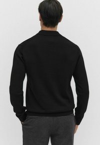 Czarny sweter z dzianiny o luźnym kroju, z okrągłym dekoltem i prążkowanymi mankietami. Miękka tekstura i minimalistyczny design.