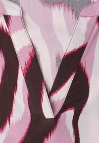 Vêtement à col en V avec motif ondulé abstrait dans des tons de rose, blanc et marron foncé, avec des bords de col cousus.