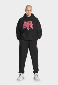 Czarny komplet z bluzy z kapturem i spodni dresowych z wyraźnym czerwonym napisem "PROSTO ATHLETIC", zapewniający komfortowe dopasowanie i elastyczne mankiety. Klasyczny styl sportowy.