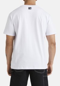 Camiseta de algodón blanca con mangas cortas, un cuello redondo y una etiqueta de marca negra en la parte posterior. Presenta una textura suave y un ajuste relajado.