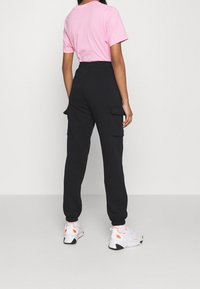 Černé cargo kalhoty s bočními kapsami, elastickými manžetami a přiléhavým pasem, doplněné růžovým tričkem s krátkým rukávem a bílými teniskami.