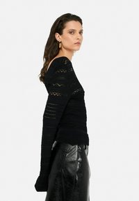 Black long-sleeve top with textured knit pattern, featuring horizontal and vertical lines. Paired with a glossy, black leather skirt.