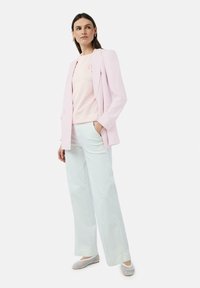 Hellrosa, taillierter Blazer über einem hellrosa Pullover, kombiniert mit weit geschnittenen weißen Hosen und geflochtenen Slippern. Glattes Material, minimalistisches Design.