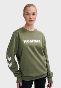 Sudadera verde oliva de algodón con cuello redondo, que presenta "HUMMEL" en texto blanco y acentos en forma de flecha blanca en las mangas.