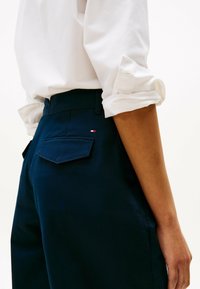 Pantaloni blu navy in cotone con una texture liscia. Caratterizzati da risvolti ai polsini, due tasche posteriori e un piccolo logo del marchio sulla tasca destra.