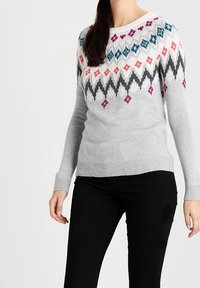 Ljusgrå tröja med ett zigzag-mönster i flera färger (rosa, teal, svart) över bröstet. Mjuk textur, ribbade muddar och nederkant.