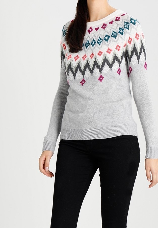 Ljusgrå tröja med ett zigzag-mönster i flera färger (rosa, teal, svart) över bröstet. Mjuk textur, ribbade muddar och nederkant.