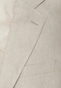 Světle béžový lněný blazer se strukturovanými klopami, jedinou kapsou a texturovanou tkaninou. Viditelná jednobarevná podšívka.