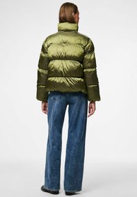 Tamsiai žalia pūkinė striukė su aukštu apykakle, pasižyminti horizontaliai siuvinėtomis dalimis ir blizgia, lygiąja tekstūra. Suderinta su plačiomis džinsinėmis kelnėmis.