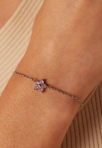 Zilveren armband met een bloemenmotief, versierd met vijf roze edelstenen en een centraal zwart accent, gedragen om een pols met een gestructureerde huid.