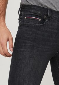 Mörkgrå denimjeans med slim fit, med en liten framficka som accentueras av röd, vit och blå sömnad. Klassisk femficksdesign.