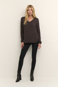 Blouse longue marron foncé à manches longues avec un décolleté en V, accompagnée d'un pantalon noir ajusté et de bottines noires à talons, présentant un design épuré et minimal.