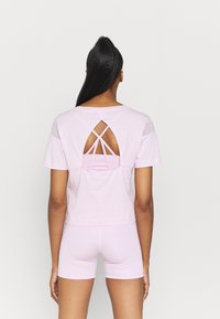 Rosa kortärmad topp med öppen rygg och ett korsad remdesign. Matchas med ljusrosa shorts. Mjuk tygtextur.