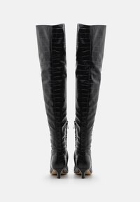Bottes hautes en cuir noir à motif crocodile, au-dessus du genou, avec une silhouette ajustée, des zips latéraux et des talons fins. Texture lisse et finition brillante.