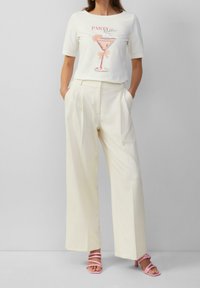 T-shirt blanc avec un graphique rose d'un verre à cocktail et le texte "PARTY". Pantalon large crème. Sandales à talons roses clairs.