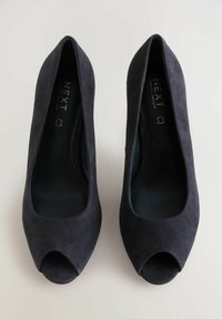 Pari di scarpe da donna nere in suede con punta aperta, marca "Next", viste dall'alto su uno sfondo neutro.
