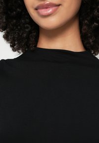Fekete, magas nyakú felső puha, rugalmas anyagból. Varrás nélküli, minimalista kialakítású, sima textúrájú, látható díszítések nélkül.