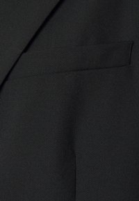 Czarna marynarka wykonana z teksturowanej tkaniny o gładkim wykończeniu. Projekt zawiera pojedynczą kieszeń na piersi po lewej stronie.