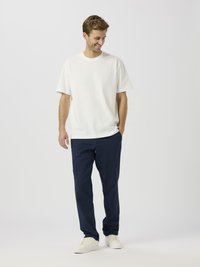 Camiseta blanca de algodón con mangas cortas, combinada con pantalones de algodón azul marino y zapatillas beige. Diseño simple, ajuste relajado.