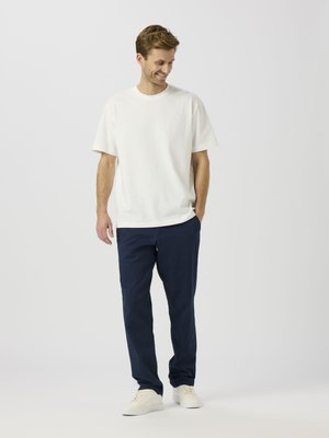 White cotton T-shirt with short sleeves, paired with navy blue cotton trousers and beige sneakers. Simple design, relaxed fit.