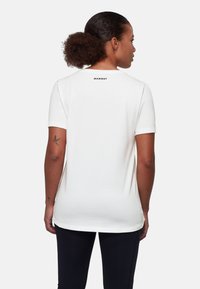 Biała bawełniana koszulka z krótkimi rękawami, okrągłym dekoltem i czarnym logo "MAMMUT" na górnej części pleców. Gładka tekstura i luźny krój.