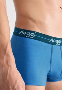 Blaue Baumwoll-Boxershorts mit einem kontrastierenden dunkelgrünen elastischen Bund mit "sloggi"-Logo. Fein vernähte Kanten und eine enganliegende Passform.