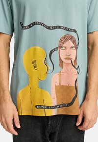 T-shirt azzurro chiaro con grafica frontale di una figura gialla e una donna, con i testi "Era un astratto perfettamente buono" e "Sei ancora qui?"