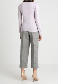 Hellblau-lila, enganliegender Pullover mit Rundhalsausschnitt und langen Ärmeln, kombiniert mit grauen karierten, cropped Hosen und beigen High Heels.
