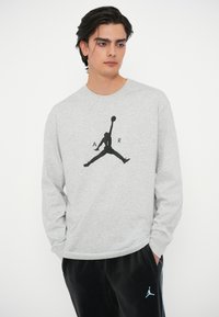 Grauer Langarm-Sweatshirt mit schwarzem Jumpman-Logo und "AIR"-Text, kombiniert mit schwarzen Hosen mit hellblauen Akzenten.