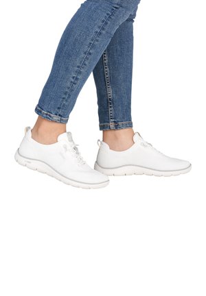 Füße mit weißen Sportsneakern und blauen eng anliegenden Jeans vor weißem Hintergrund.