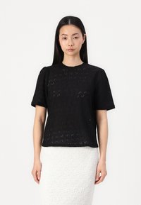 Svart kortermet topp med teksturert, mønstrete design med diamantformer. Rett snitt og rund hals. Glatt stoff med lett gjennomsiktighet.