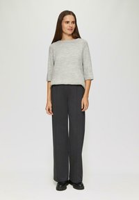 Helle graue Strickpullover mit weitem Ausschnitt und Dreiviertelärmeln, kombiniert mit dunkelgrauen weiten Hosen und schwarzen klobigen Schuhen.
