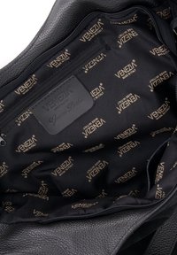 Interieur van een zwarte leren tas met een soepele textuur en een herhalend "Venezia" logo patroon in goud op zwarte stof. Inclusief een ritsvak.