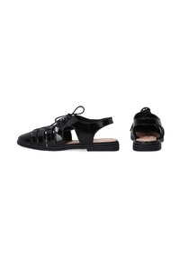 Zwarte gepatineerde leren sandalen met een open teen, crisscross ontwerp en verstelbare veters; heeft een platte zool en uitsnijdingen aan de zijkanten.