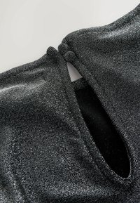 Top metalizat negru, cu un material texturat și strălucitor. Detaliile cu tăieturi duble la spate și o mică deschidere creează un design unic.