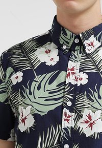 Tričko s krátkým rukávem v námořnické modři s tropickým květinovým potiskem se bílými květy a zelenými listy. Bavlněná látka s předn�ím zapínáním na knoflíky.
