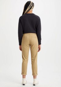 Sweatshirt noir court, chinos kaki avec des revers, et baskets montantes blanches ; tissu lisse avec des détails de couture minimaux.