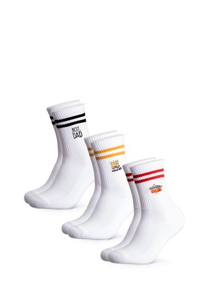 Weiße Sportsocken mit zwei roten Streifen und "Super Dad"-Emblem, getragen zu hochgekrempelten blauen Jeans an den Beinen einer sitzenden Person vor weißem Hintergrund.