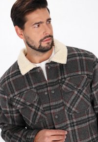 Gråternet flanneljakke med krèmefarvet sherpa-krave, som har to brystlommer og knaplukninger. Strukturérmateriale med røde accenter.