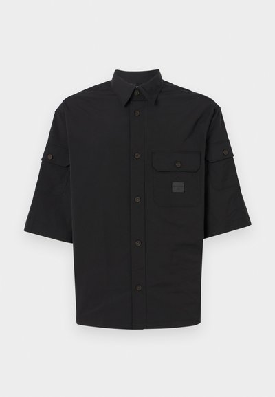 Lyhythihainen musta paita kevyestä kankaasta. Omaavat napituskauluksen, kaksi etutaskua ja pienen logopatchin.