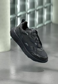 Scarpa da ginnastica atletica nera con tomaia in tessuto strutturato, dettagli lisci e suola in gomma a motivo. Dotata di sistema di allacciatura e marchio.