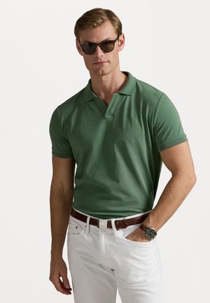 Groene poloshirt met korte mouwen, textuurstof, een knoopsluiting met twee knopen en een geborduurd logo; gecombineerd met witte broek en een bruine riem.