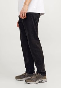 Black denim jeans with a straight-leg cut, next to gray sneakers with a combination of suede and mesh material, textured laces visible.