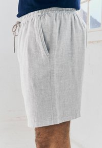 Shorts en lin gris clair avec une taille élastique et un cordon de serrage, présentant des poches latérales et une finition en tissu texturé.
