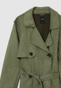 Miętowy zielony płaszcz treningowy z faux zamszu, z podwójnym zapięciem, dużym kołnierzem i paskiem. Posiada czarne guziki i gładką teksturę.