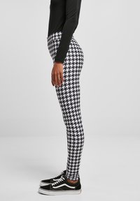 Leggings avec un motif pied-de-poule noir et blanc, en matériau extensible, associés à des baskets noires avec des accents blancs.