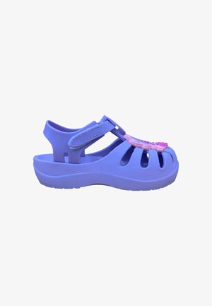 Sandalo viola per bambini con cinturino regolabile, design con punta aperta e fiore decorativo rosa sulla parte superiore, mostrato di lato su sfondo bianco.