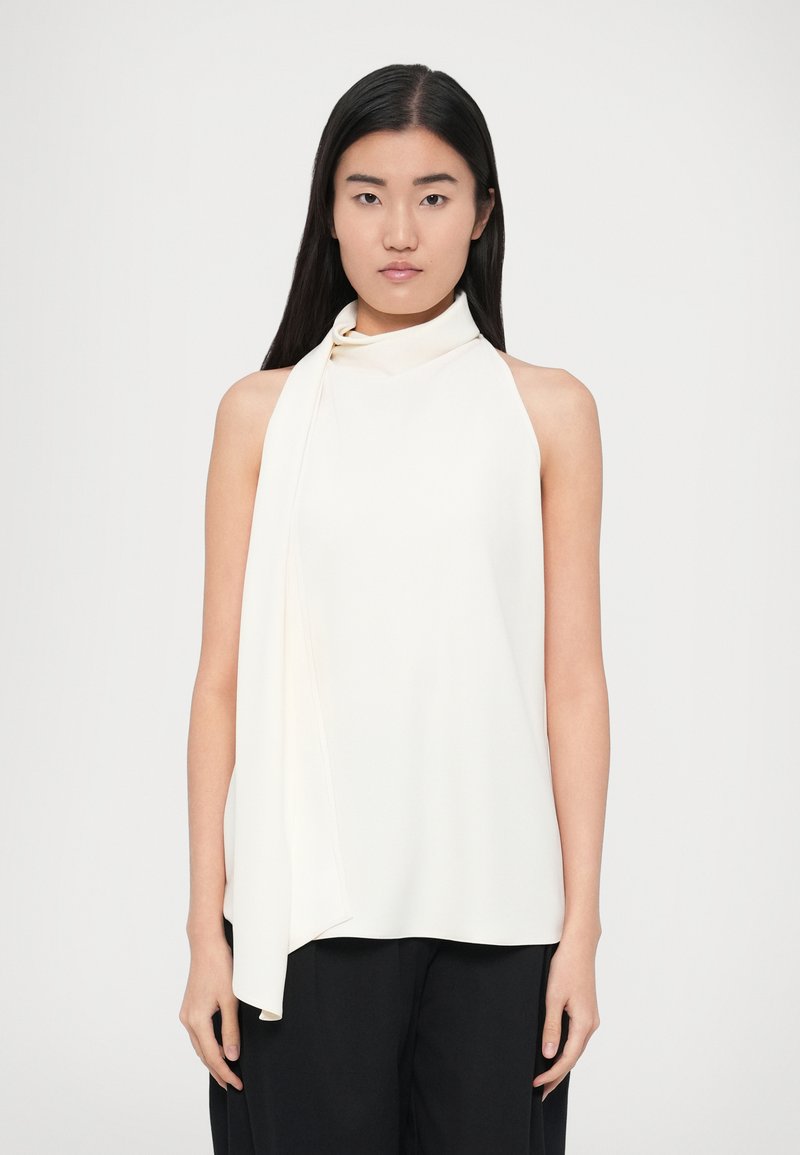 Krēmkrāsas haltera tipa tops ar plūstošu šalles detaļu uz pleca, gludu tekstūru un brīvu piegriezumu, kombinēts ar melnām platām biksēm.